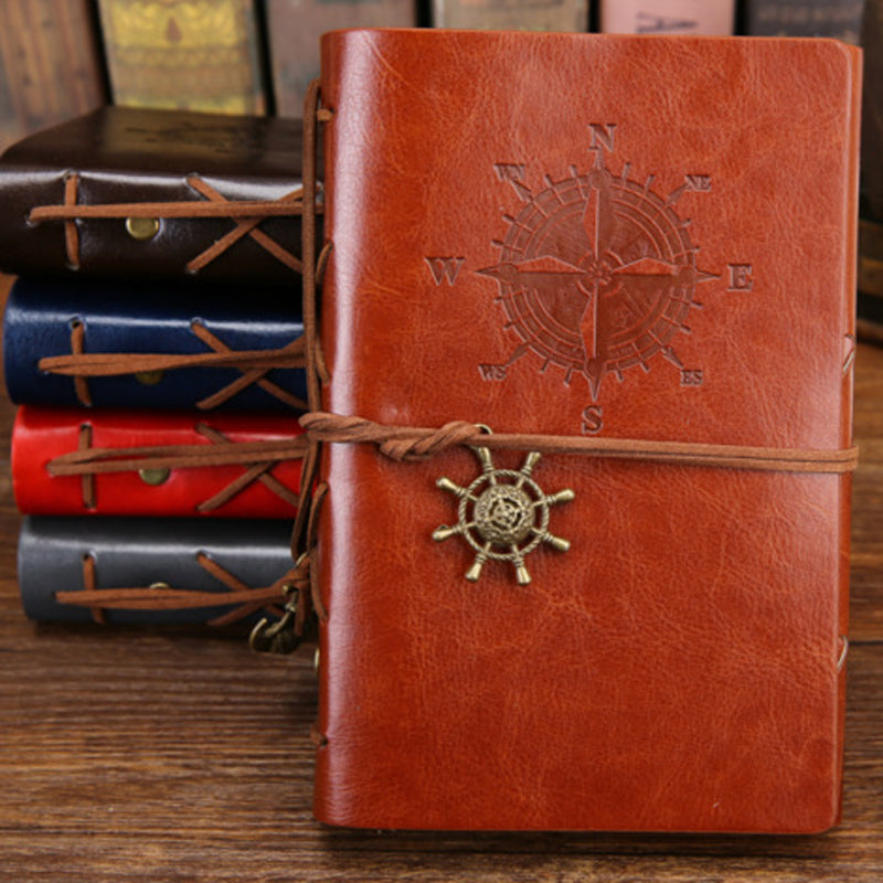 Brown leather notebook with compass design and rope, surrounded by other notebooks.